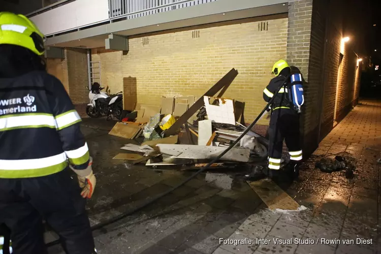 Brandweer blust stapel grofvuil tegen muur van flat